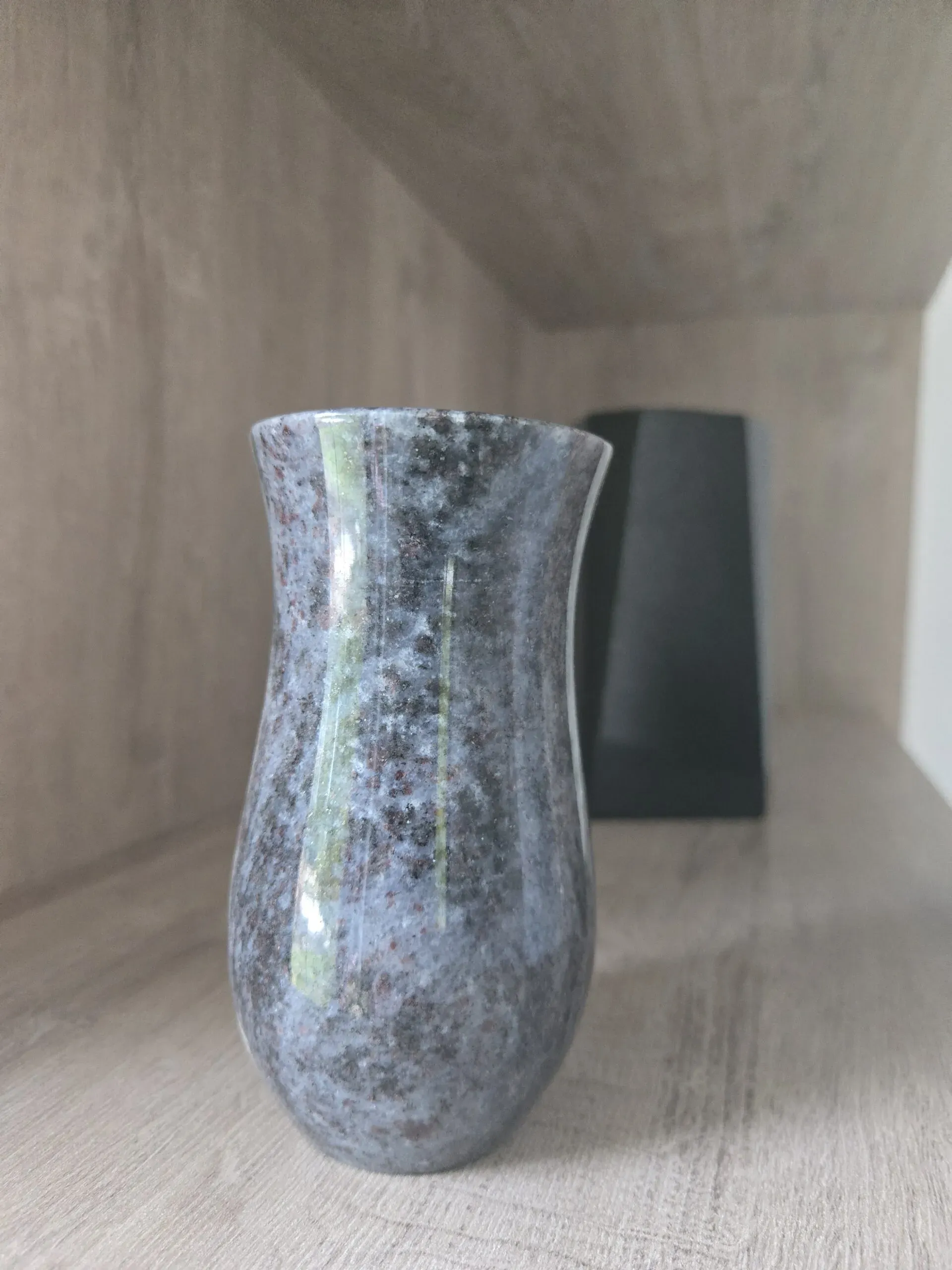 Vase funéraire en granite marbré posé sur une étagère en bois.