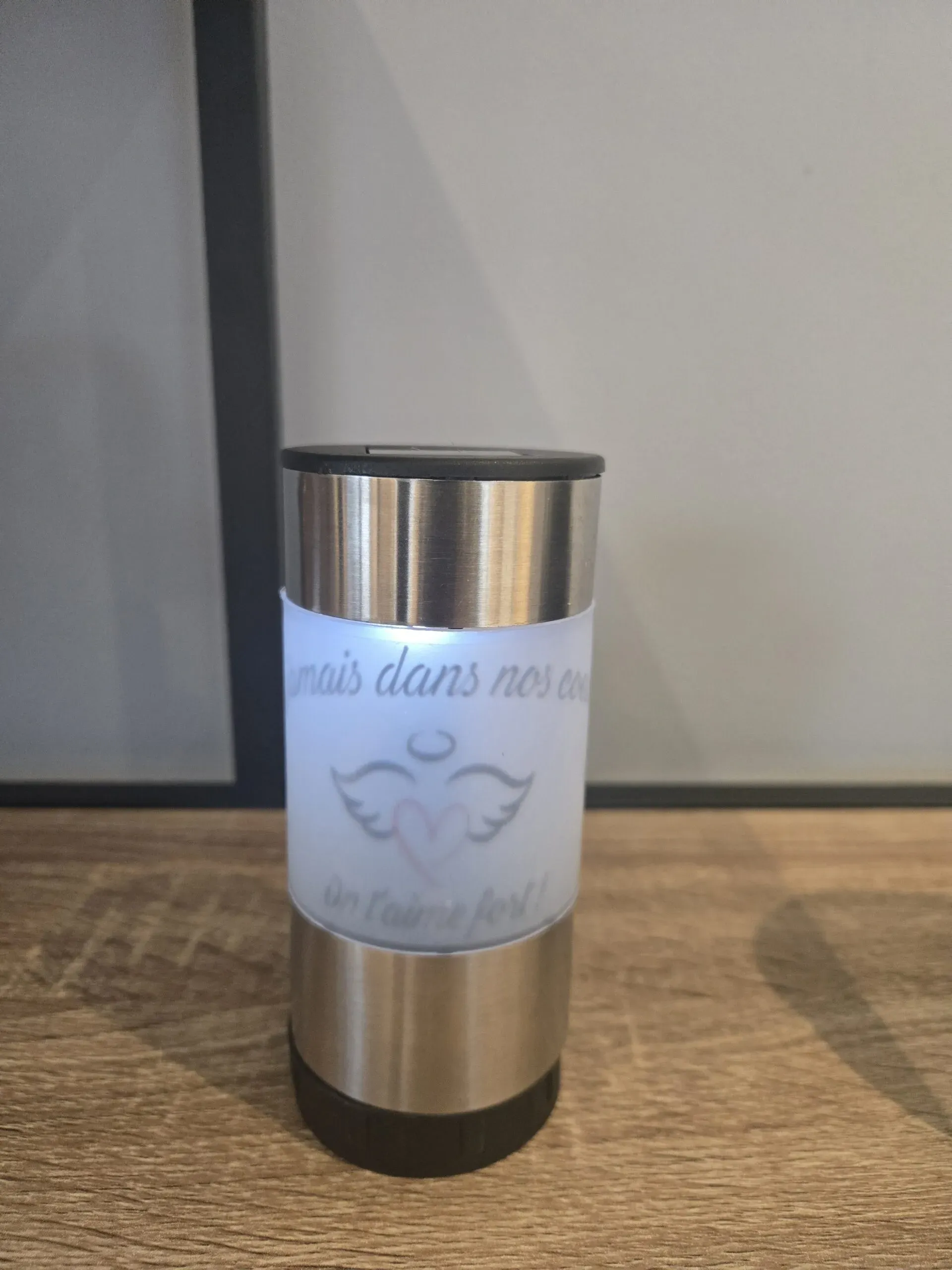 Lanterne funéraire cylindrique en acier inoxydable avec motif d'ange et message d'hommage.