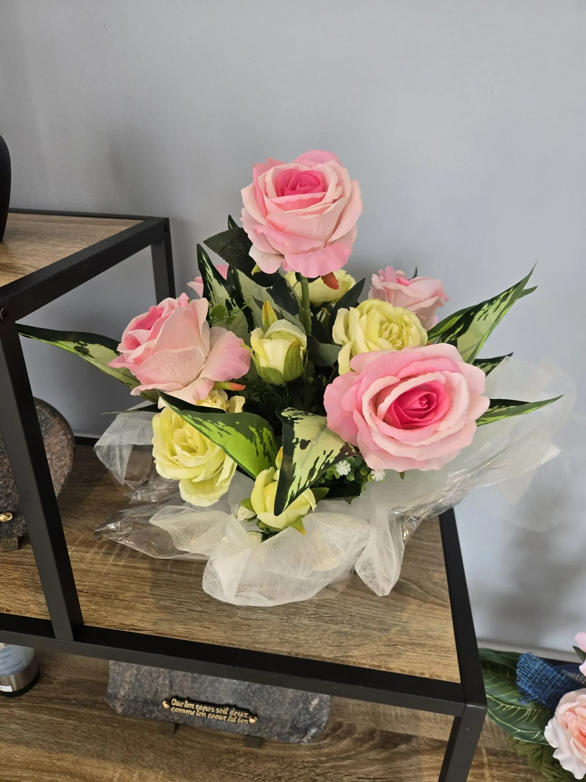 Bouquet de roses artificielles rose et jaune présenté dans un emballage transparent.