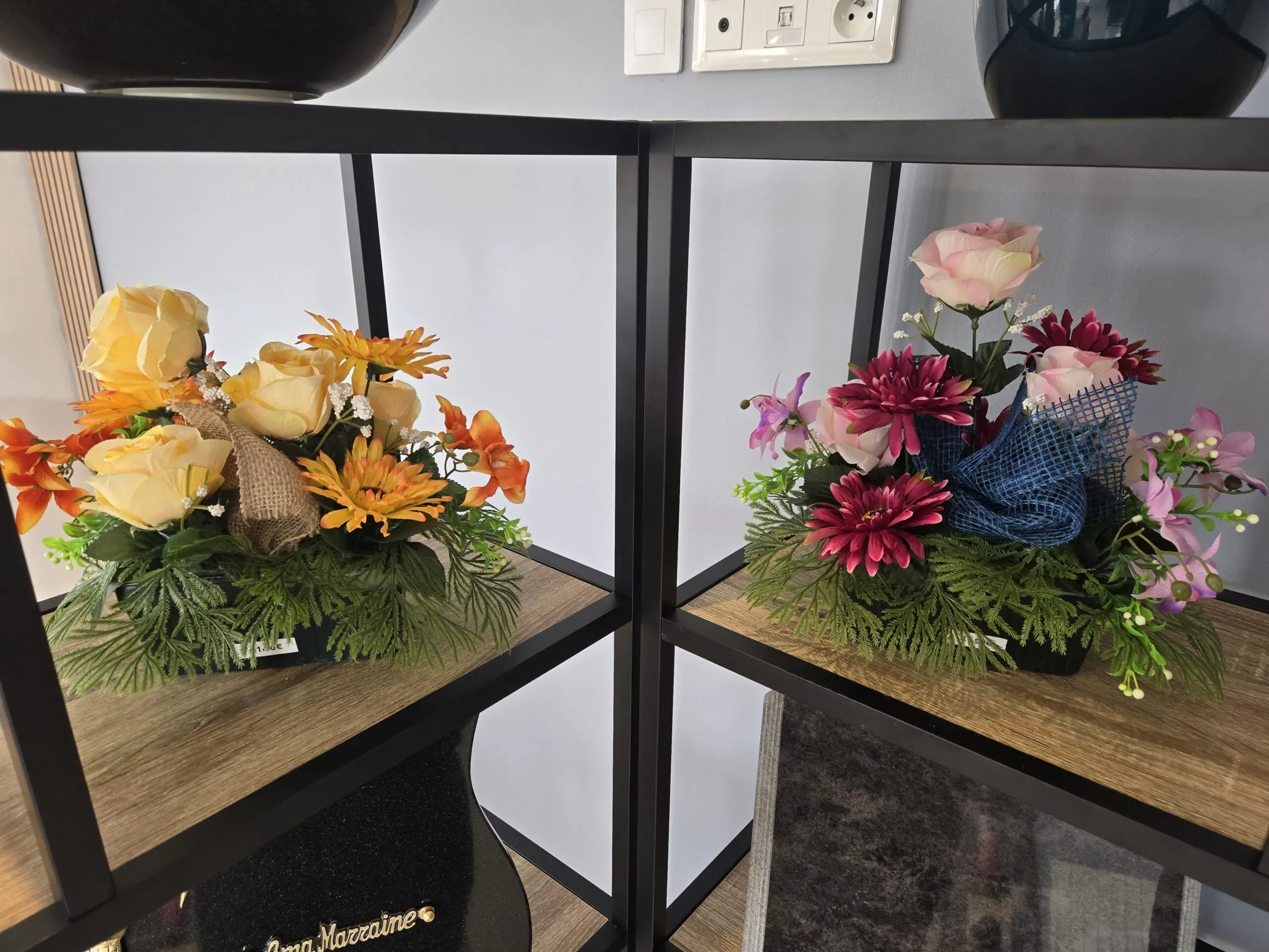 Arrangements floraux artificiels de deuil disposés sur des étagères.