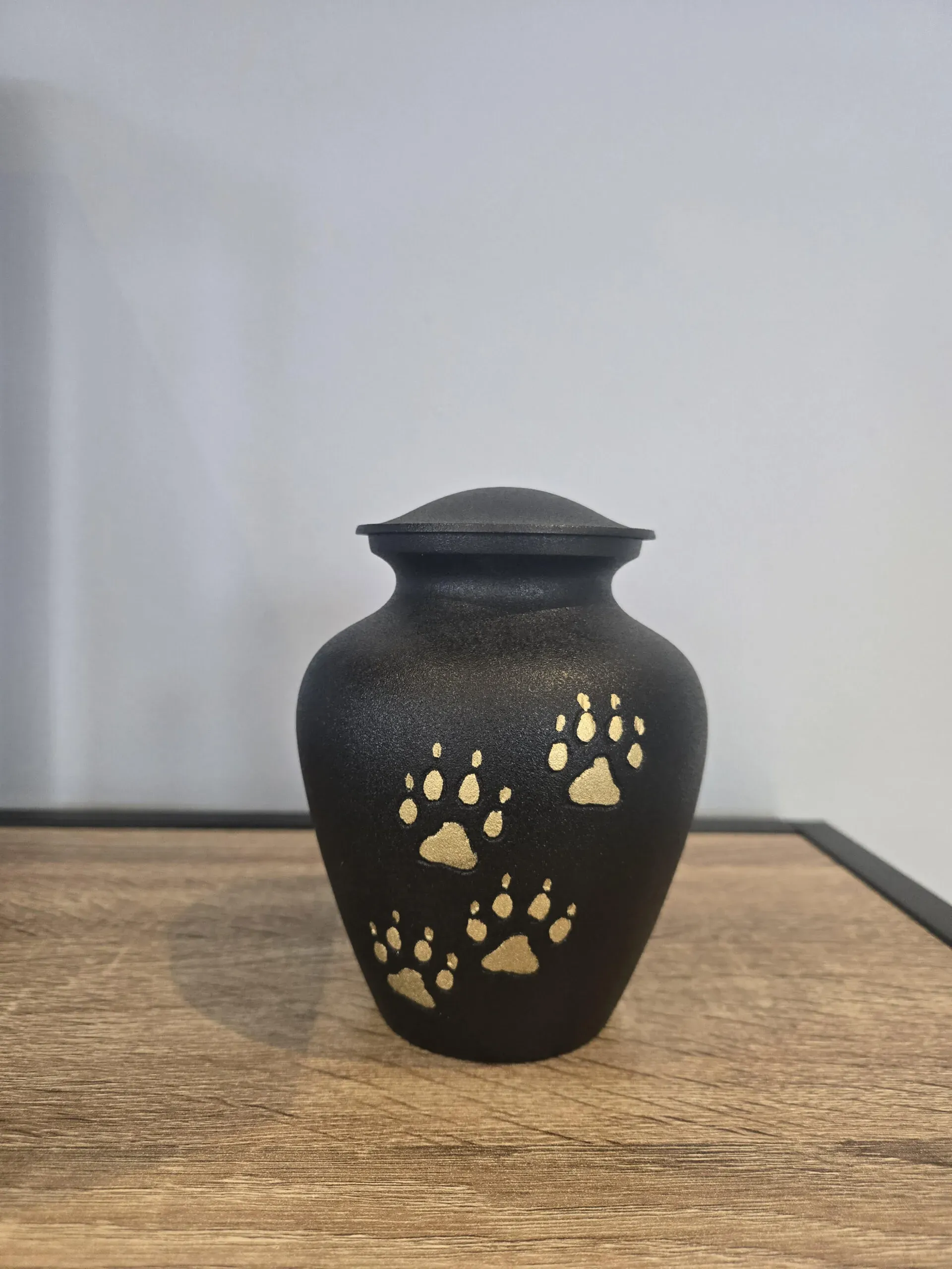 Urne cinéraire noire mate décorée d'empreintes de pattes dorées.