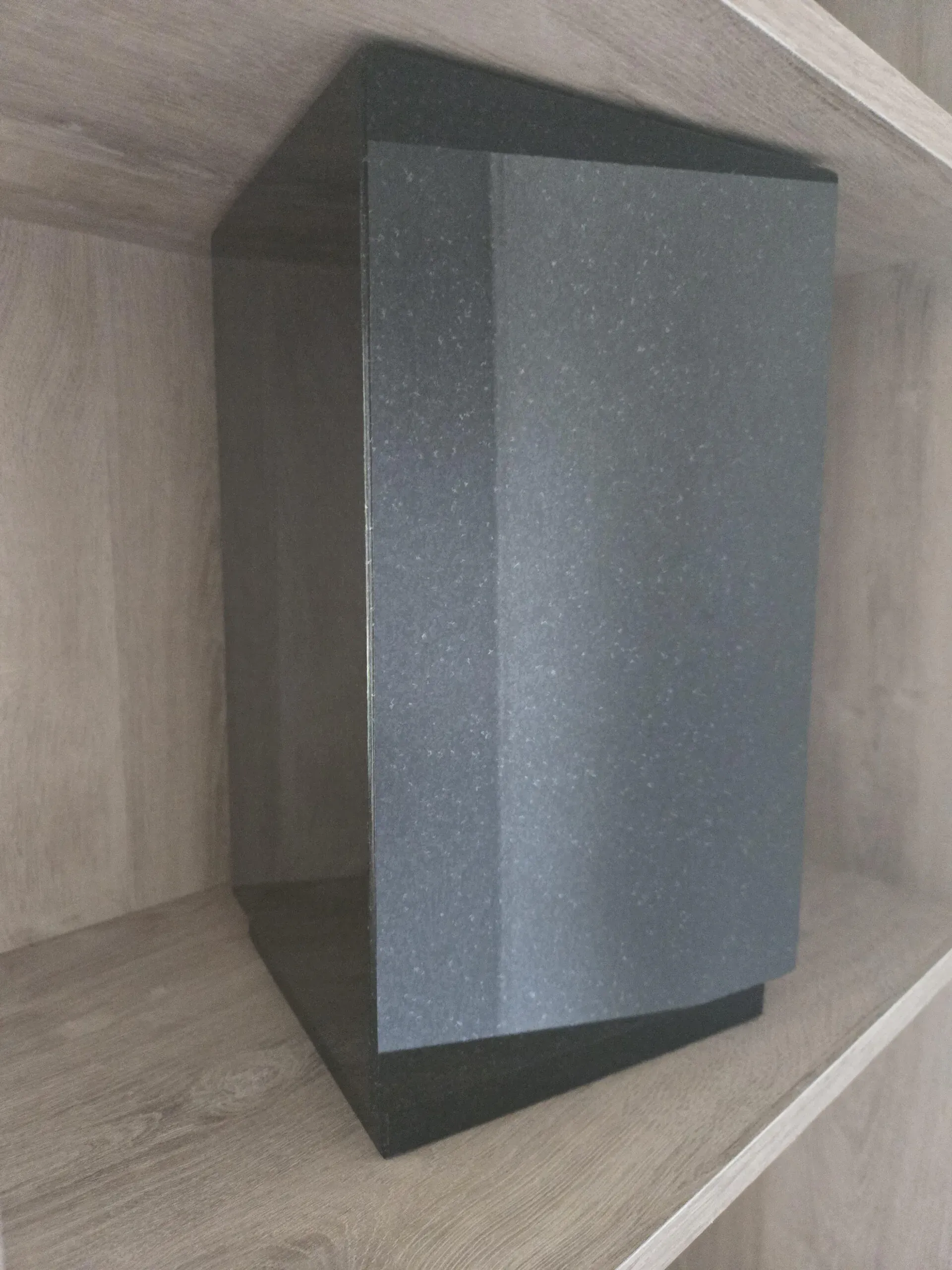Urne funéraire cinéraire en granite sombre exposée sur une étagère en bois